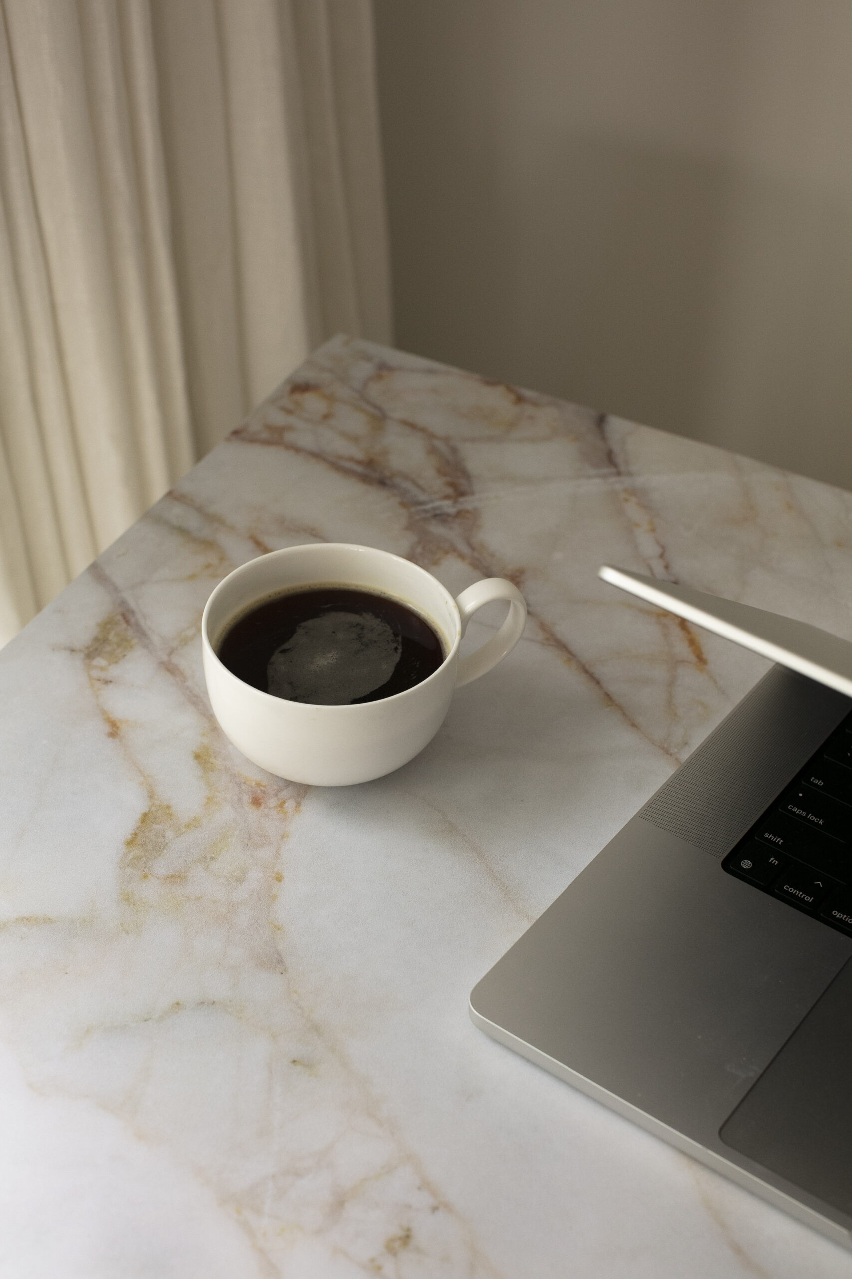 Laptop and white coffee mug on a white and tan marble table