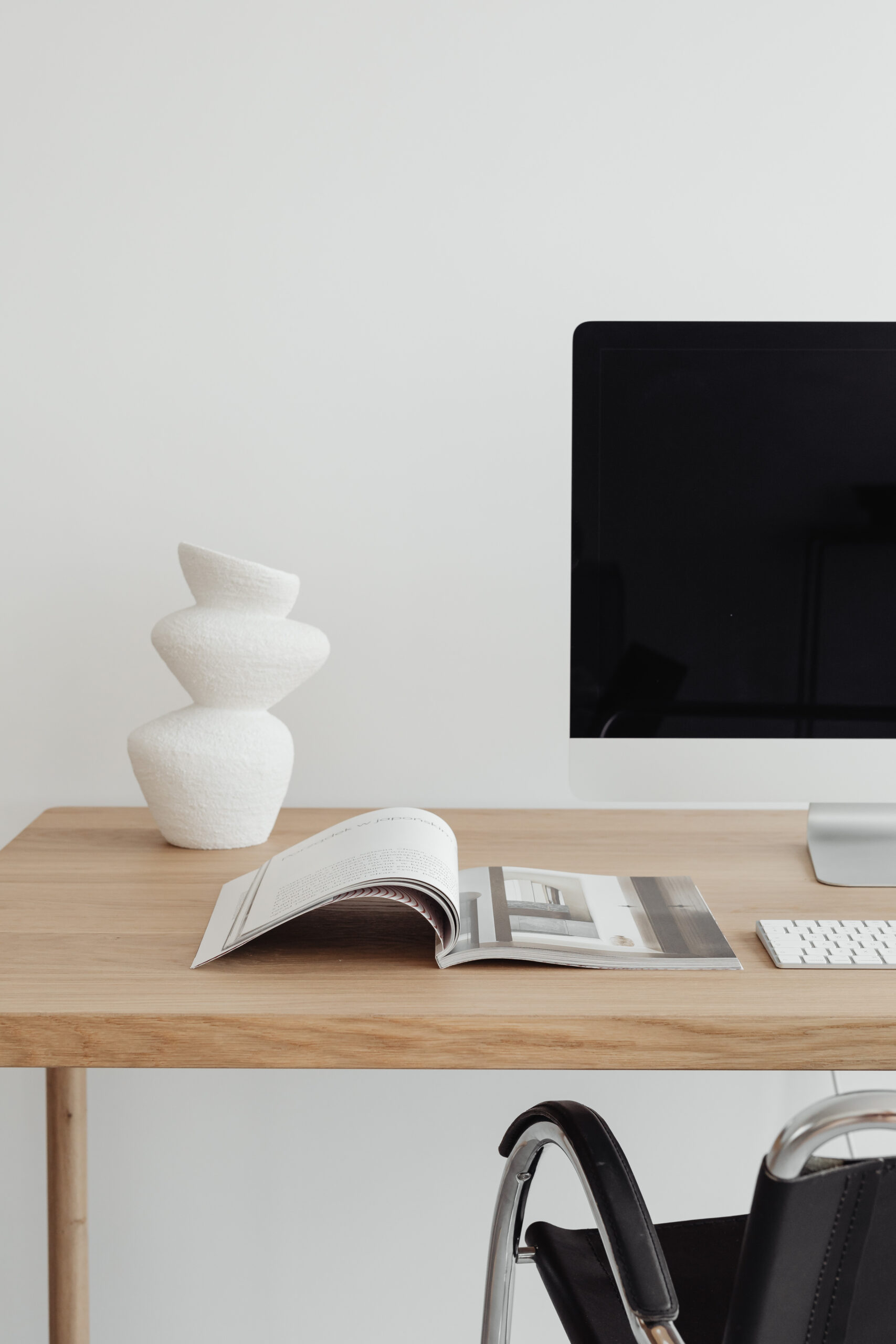 iMac and magazine on a wooden desk with an abstract white vase