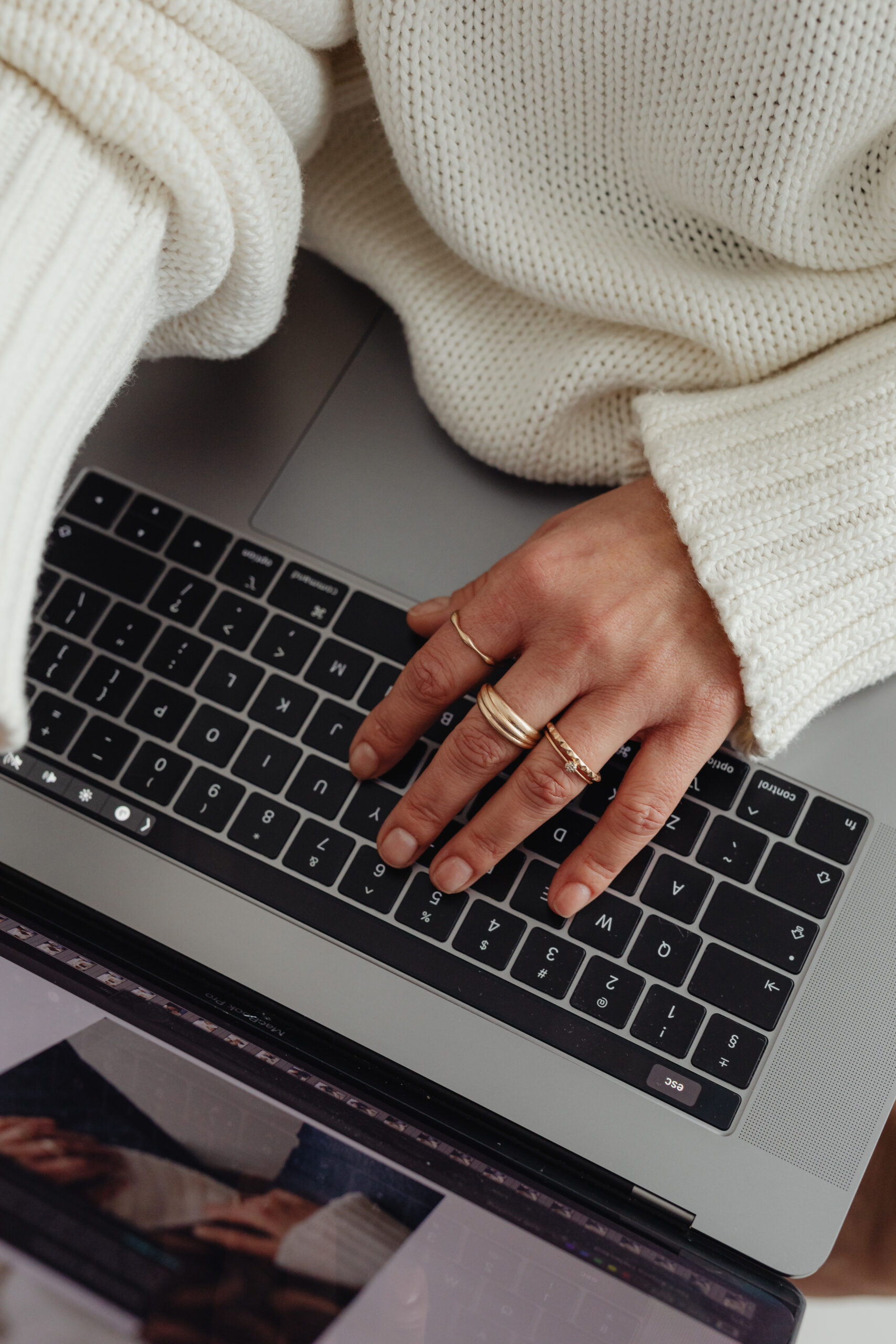 Woman in white sweater typing on a MacBook laptop