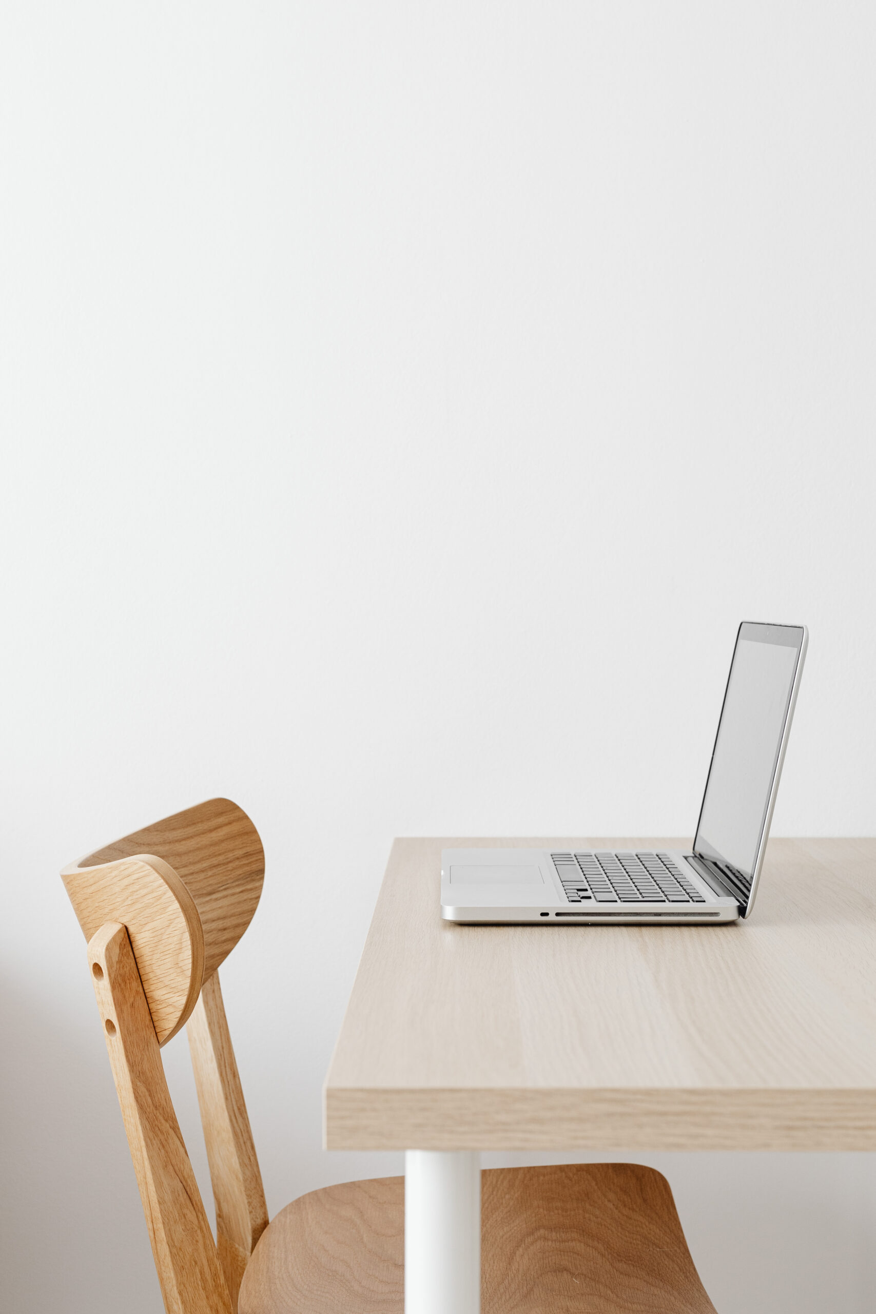 Laptop on a light wooden desk with a wood chair